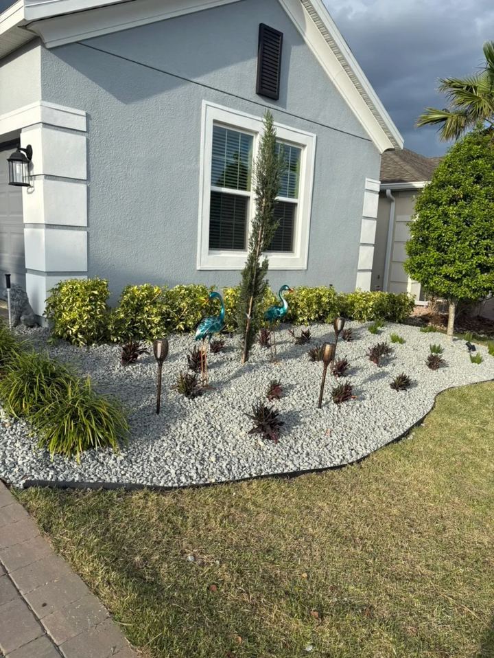 Curved bed with white rock, red-leaf plants and garden lights along the side of a house
